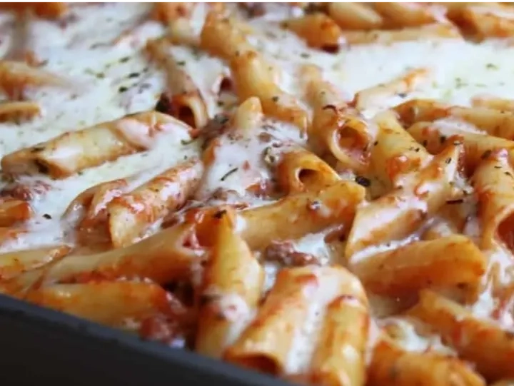 Close-up of baked ziti pasta covered in melted cheese and tomato sauce, topped with herbs in a casserole dish.