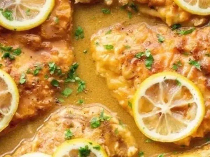 Chicken cutlets in a golden sauce, garnished with fresh parsley and topped with lemon slices.
