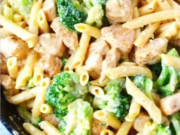 A close-up of penne pasta mixed with broccoli florets and chunks of chicken in a creamy sauce.
