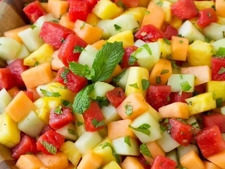 A bowl of mixed fruit salad with watermelon, cantaloupe, honeydew, and pineapple cubes, garnished with chopped mint leaves.