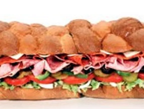 A large sub sandwich filled with layers of sliced deli meats, cheese, lettuce, tomato, green peppers, and black olives on braided bread.