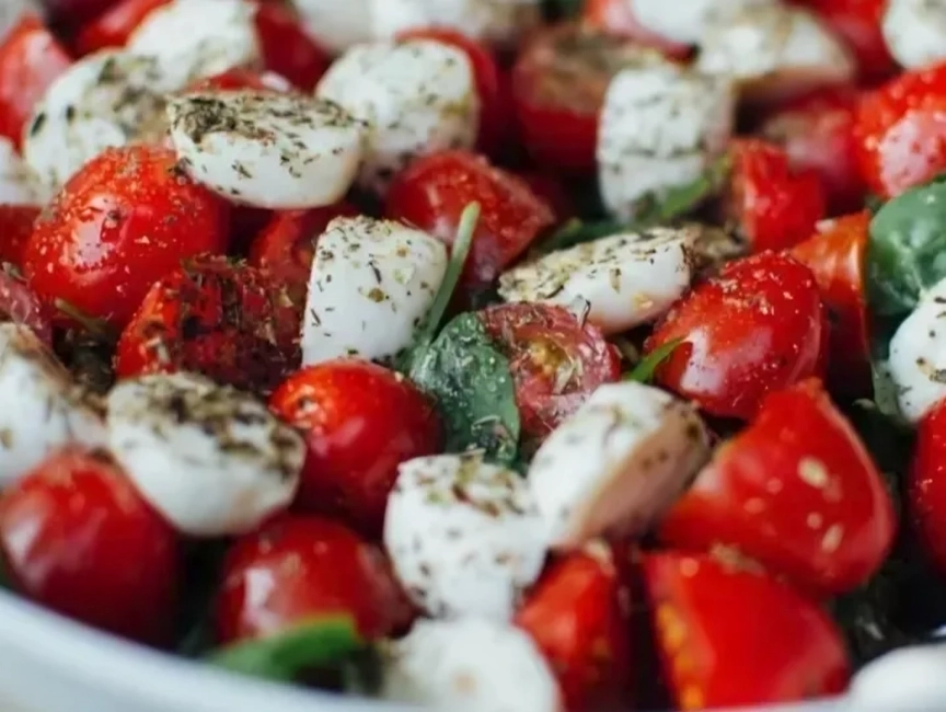 A close-up of a tomato, mozzarella, and spinach salad, topped with dried herbs and seasoning.
