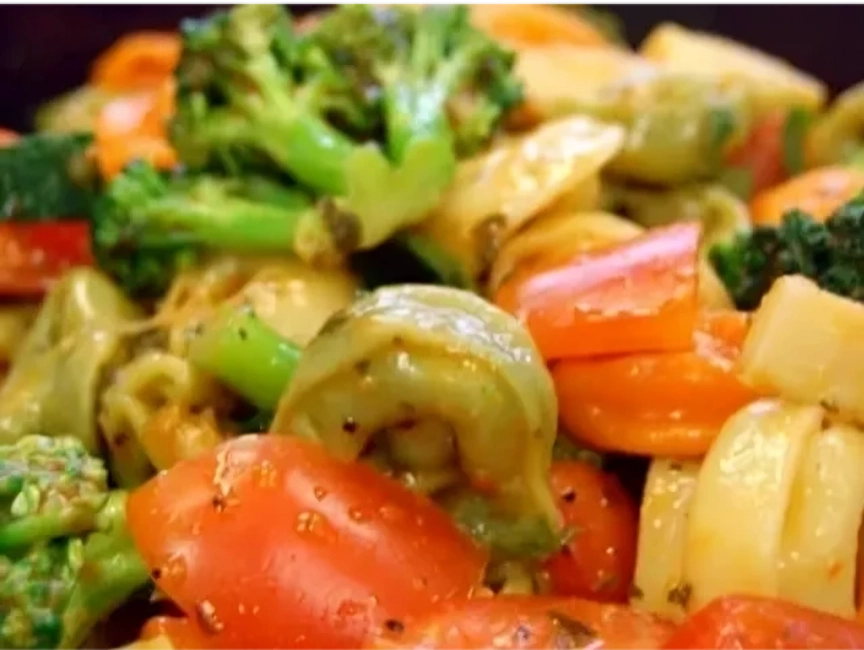 Close-up of cooked tortellini pasta mixed with broccoli, red bell peppers, and sliced carrots coated in a light sauce.