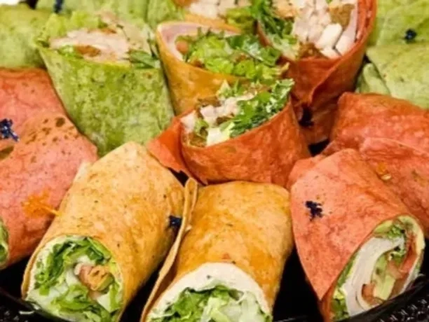 An assortment of colorful tortilla wraps filled with lettuce, vegetables, and various meats, arranged closely together on a platter.